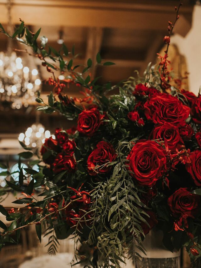 a vase filled with red roses on top of a table next to a chandelier