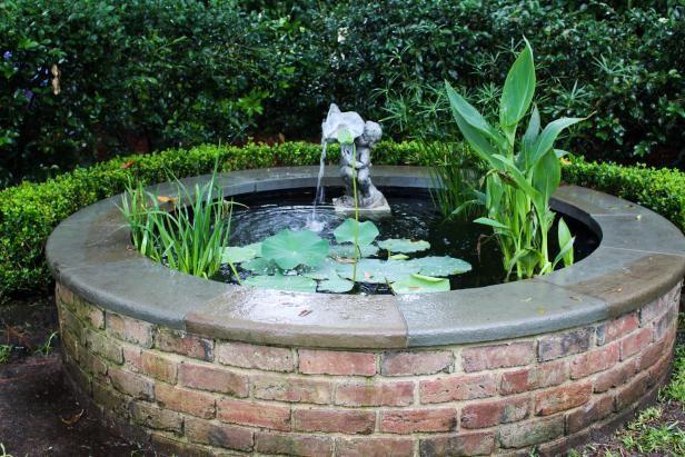 a water fountain in the middle of a brick planter filled with lily pads and greenery