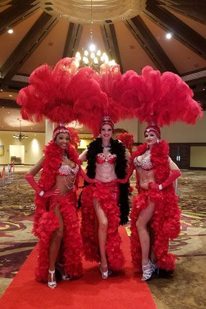 three women dressed in red and black are standing on a red carpeted area with chandeliers hanging from the ceiling