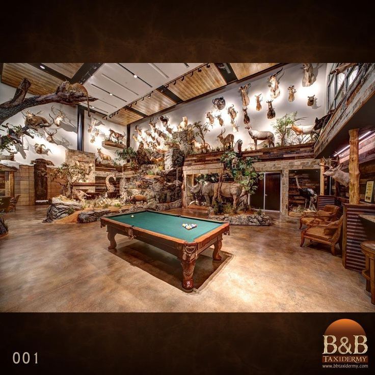 a pool table in the middle of a room with many deer heads hanging from the ceiling