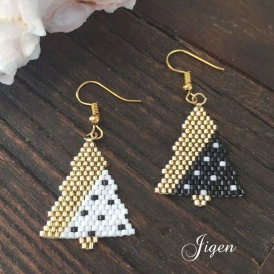 two triangle shaped beaded earrings sitting on top of a wooden table next to flowers