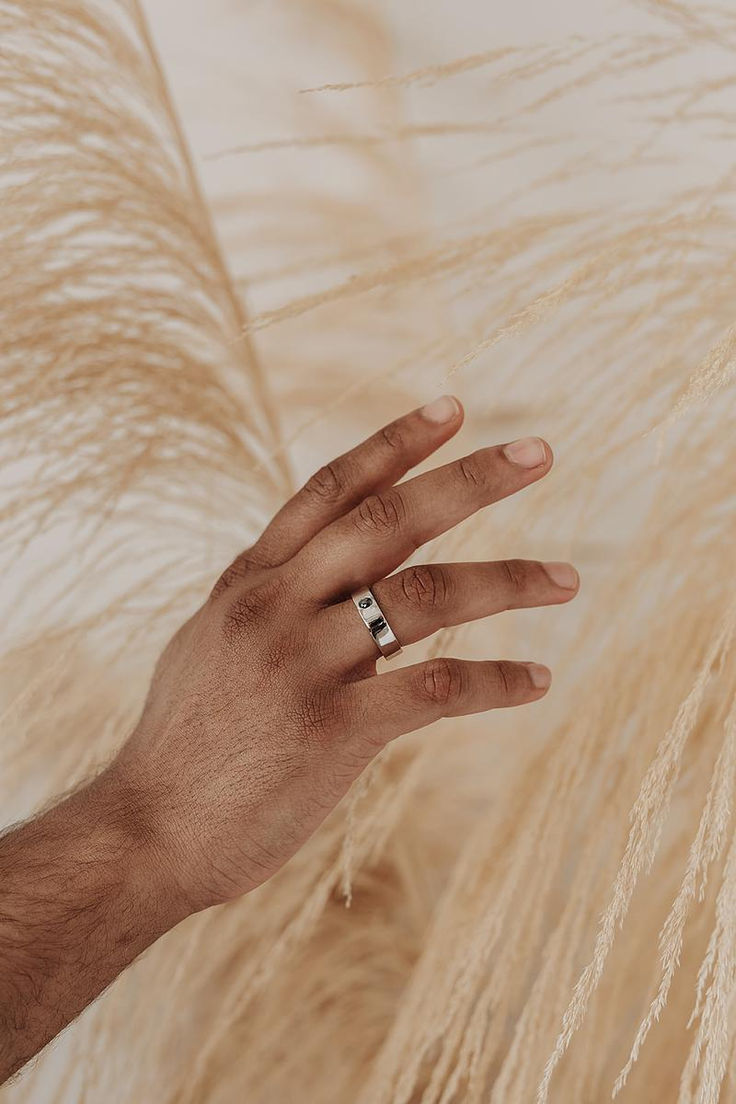 a person's hand with a wedding ring on top of some white feathers in front of them