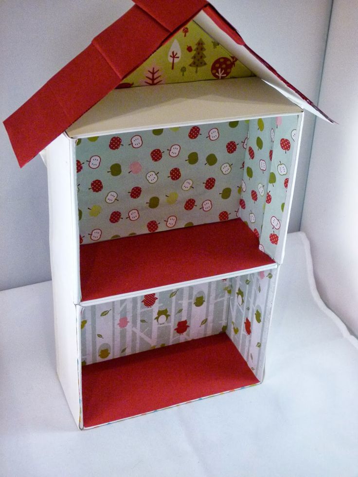 a doll house made out of paper on a white surface with a red ribbon hanging from the roof