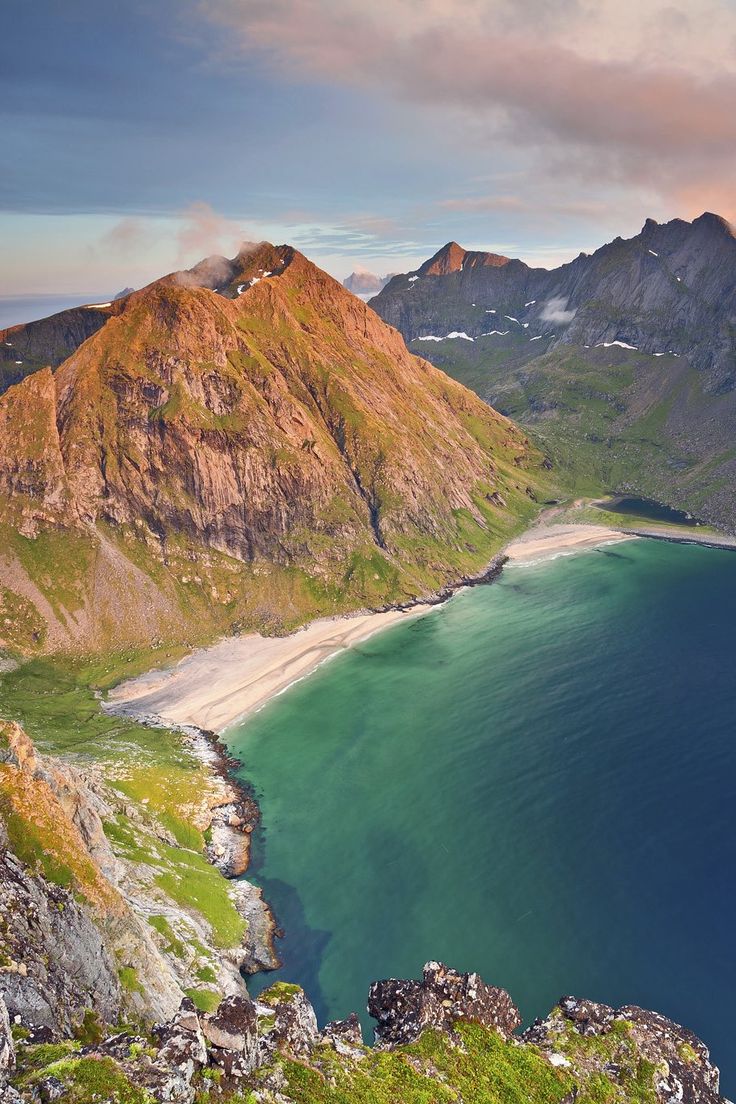 the mountains are covered in green grass and blue water, with a sandy beach below