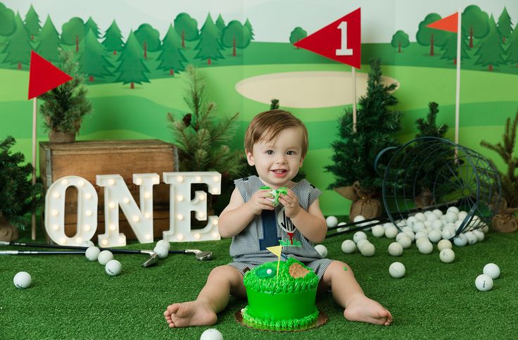 a young boy sitting on the ground with a cake in front of him and golf balls all around him