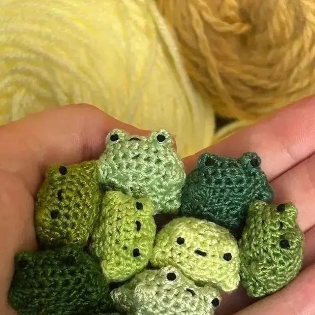 small crocheted frog amigurt toy sitting in the palm of someone's hand