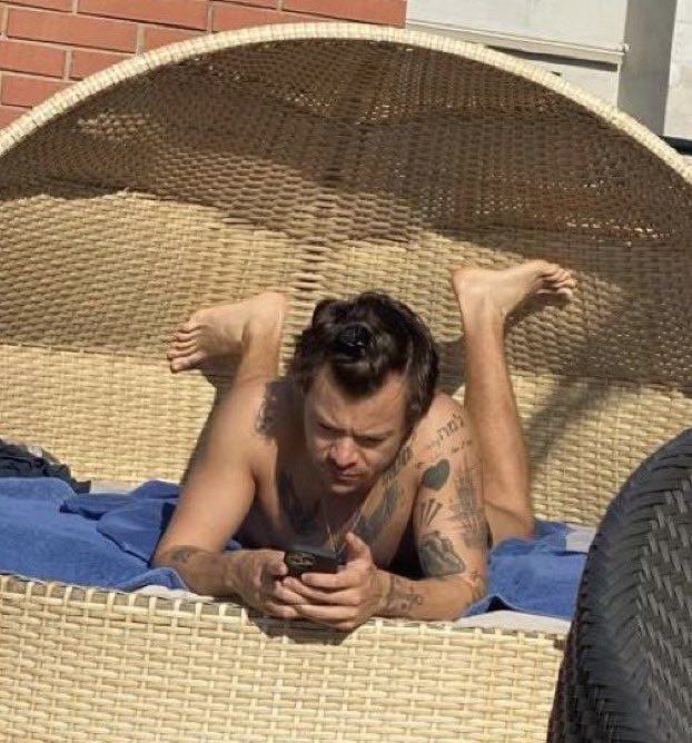 a man laying on top of a wicker chair next to a woman holding a cell phone