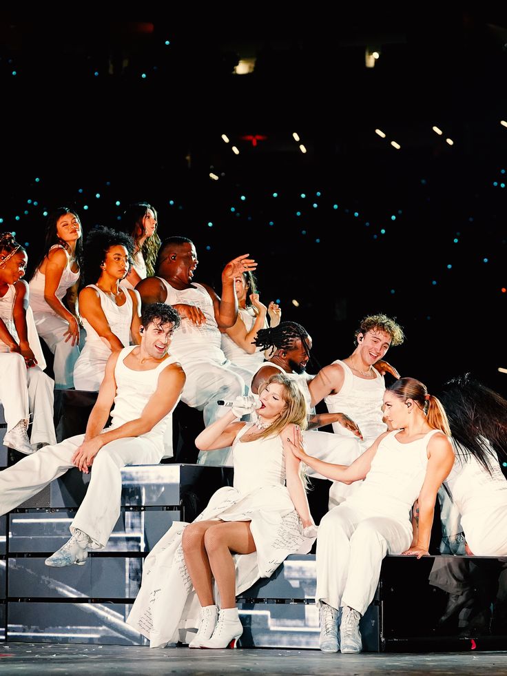 a group of women in white dresses on stage with their arms around each other as they dance