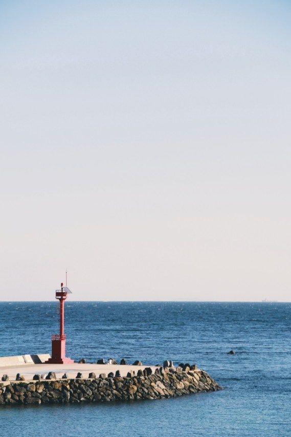 a red light house sitting on top of a pier next to the ocean in front of a blue sky