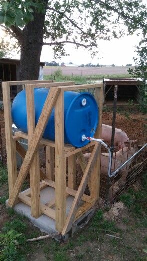 a large blue barrel sitting on top of a wooden structure next to a tree and fence