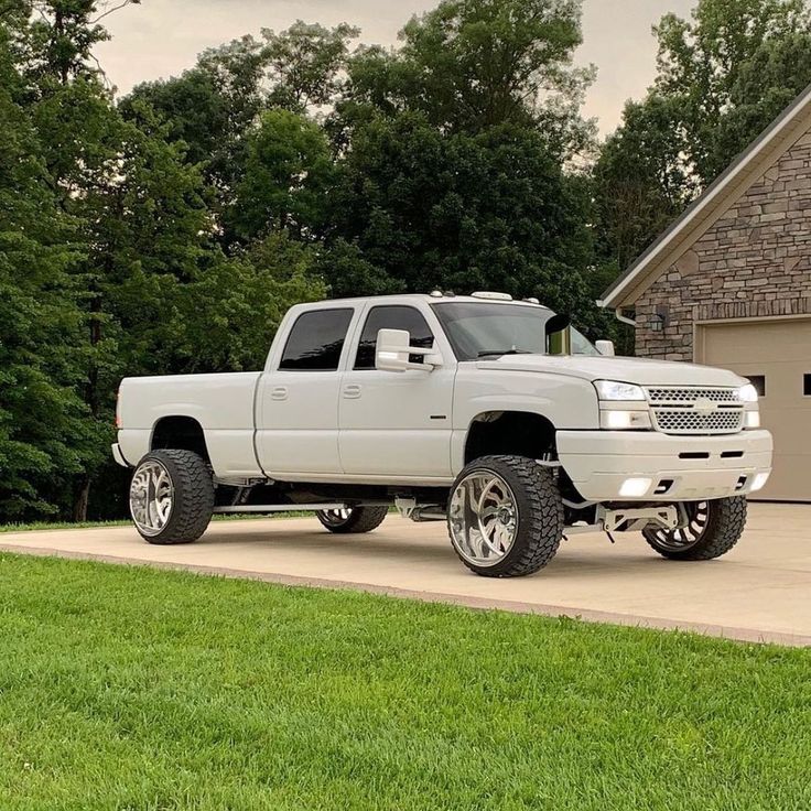 a white pickup truck parked in front of a house with large tires on it's rims