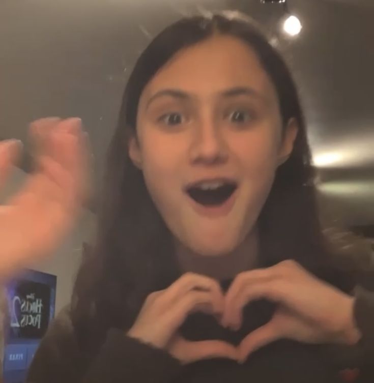 a woman making a heart shape with her hands in front of her face while another person holds out their hand to the camera