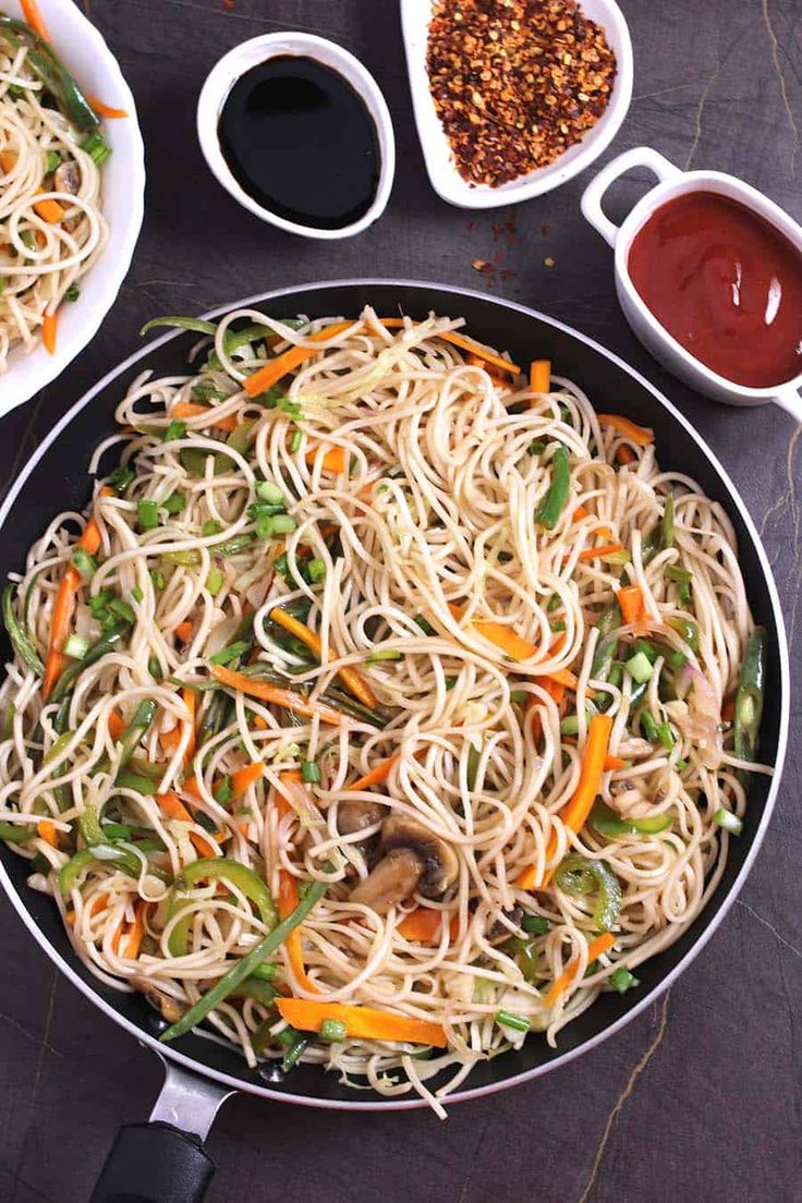 a pan filled with noodles and vegetables next to sauces