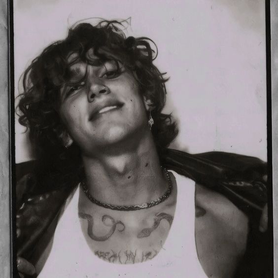 an old photo of a young man with tattoos on his chest and arms, wearing a white tank top