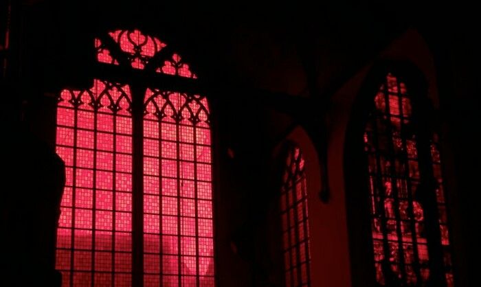 red light shining through two windows in a dark room with stained glass panels on the walls