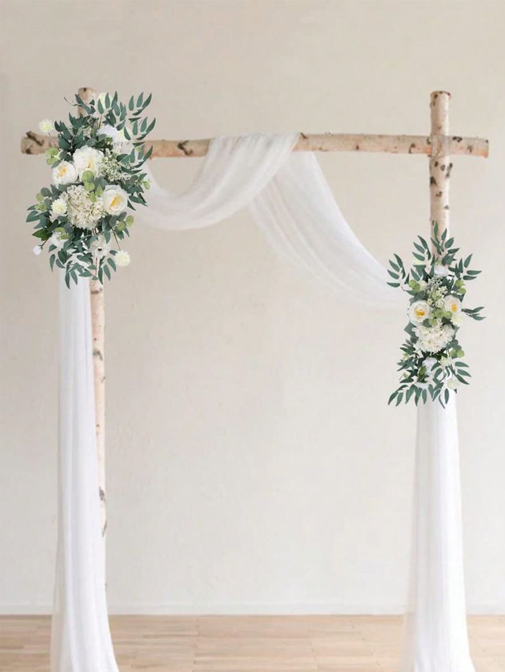 an arch decorated with white flowers and greenery for a wedding ceremony in the middle of a room