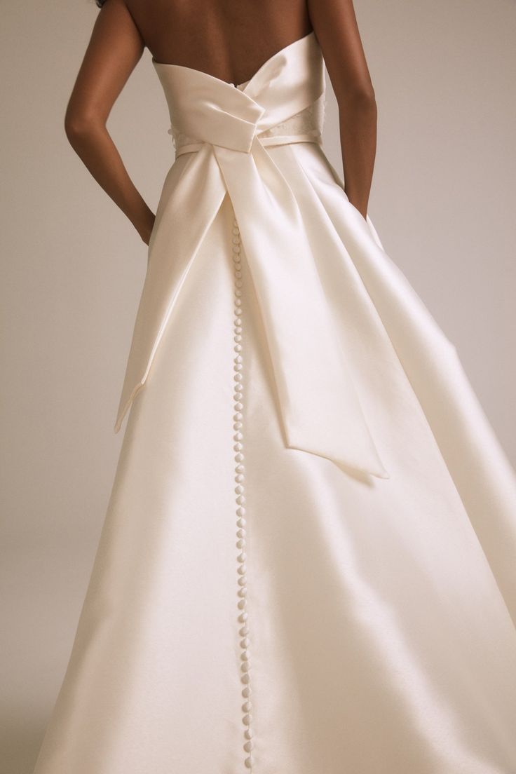 a woman in a white wedding dress with a large bow on the back of it