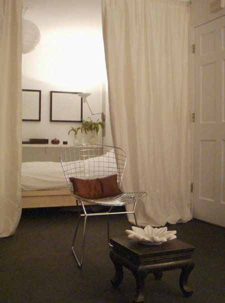 a bedroom with white curtains and a chair in the corner