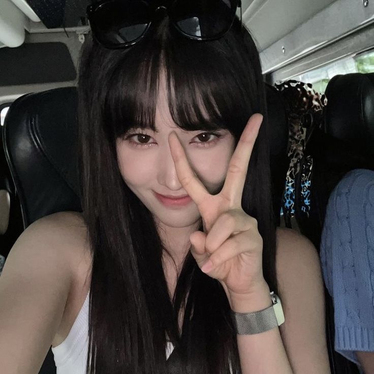 a woman with long black hair and sunglasses making the peace sign while sitting in a car