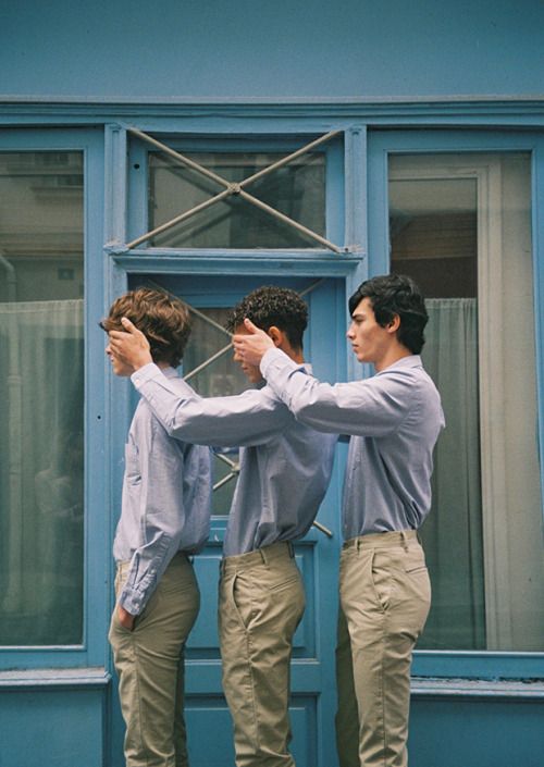 three men standing in front of a blue building with their arms around each other's shoulders