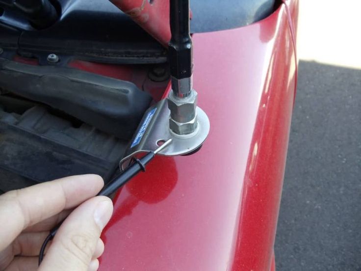 a person is holding a wrench in front of a red car