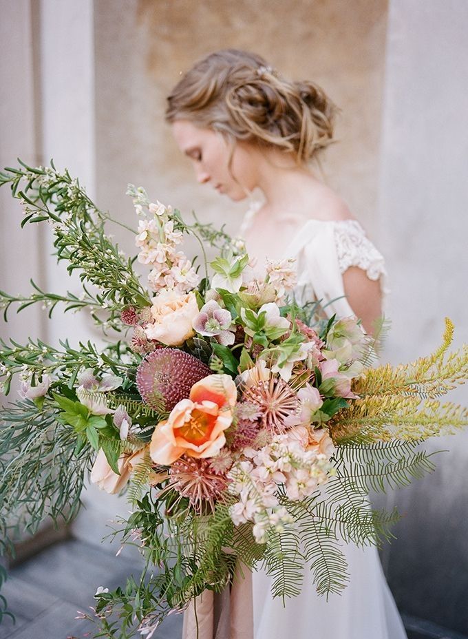 a woman holding a bouquet of flowers and greenery in front of a building wall