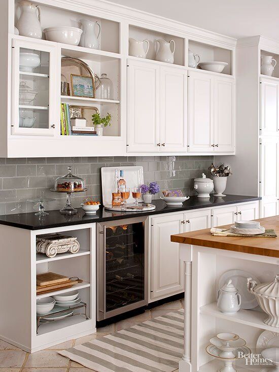 a kitchen with white cabinets, black counter tops and an open wine cooler in the corner