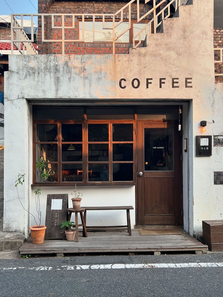 the entrance to a coffee shop with two benches and potted plants on the porch