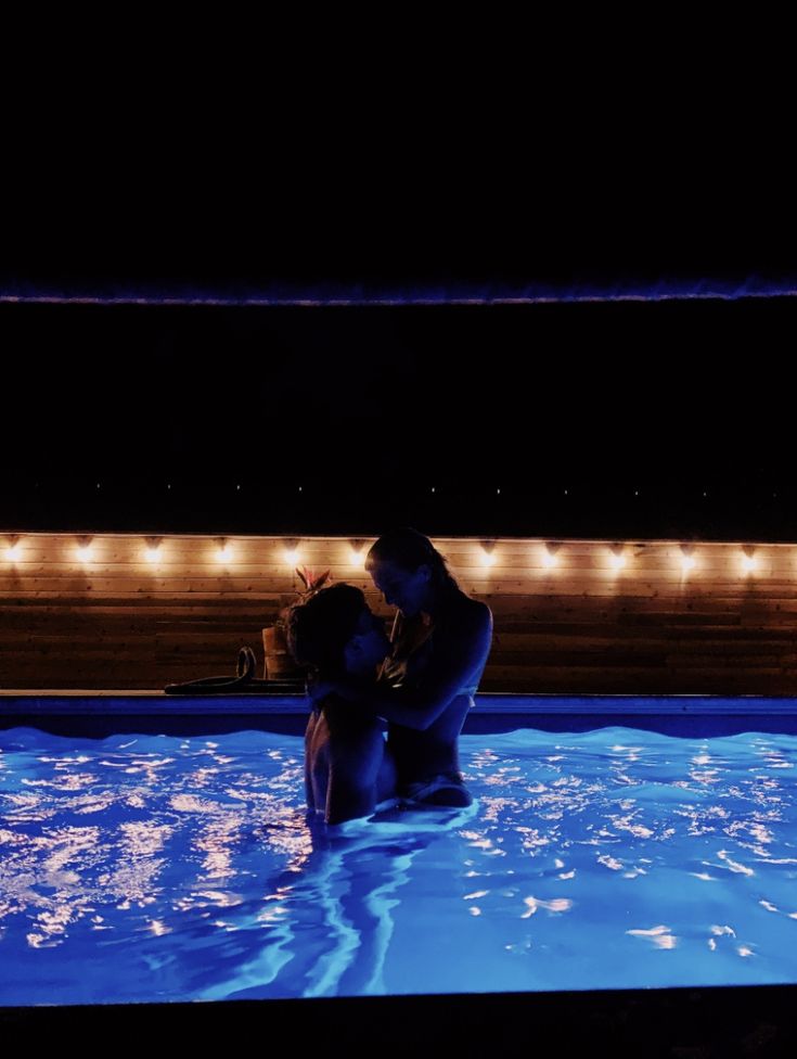 a man and woman kissing in the pool at night