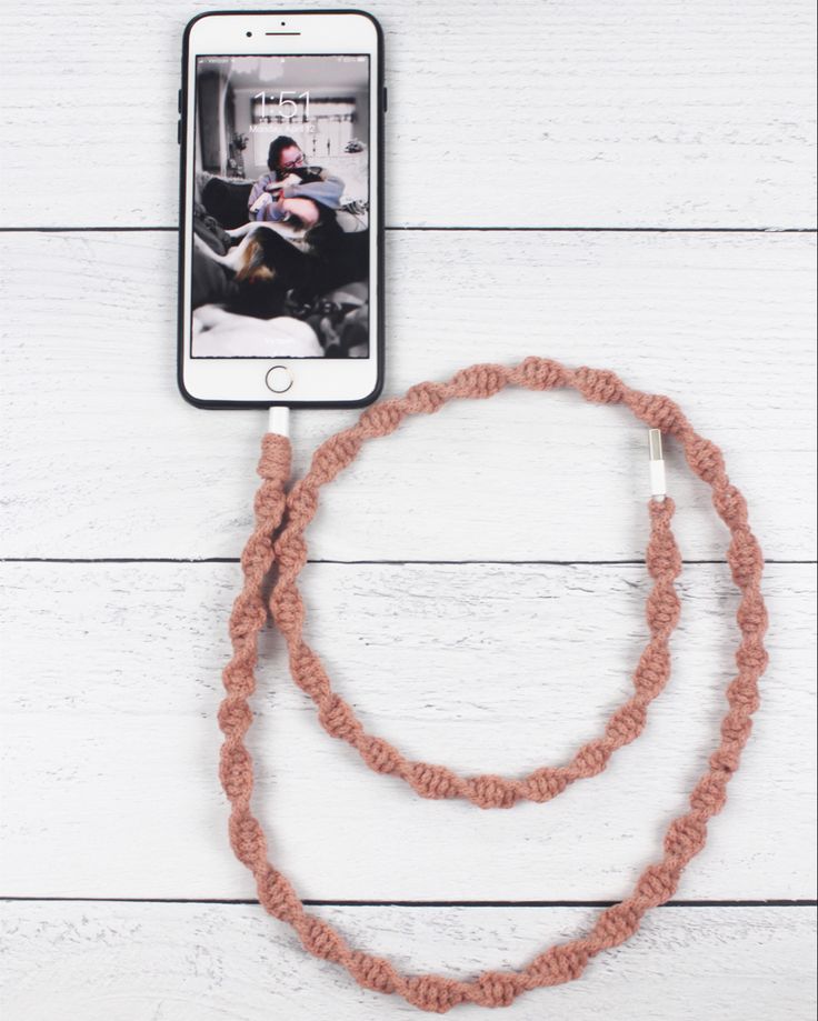 a cell phone is hooked up to a rope on a white wooden surface with an orange cord