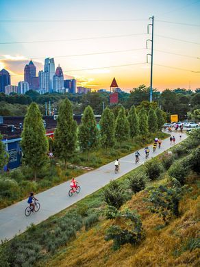 many people are riding bikes down the road in front of some tall buildings and trees