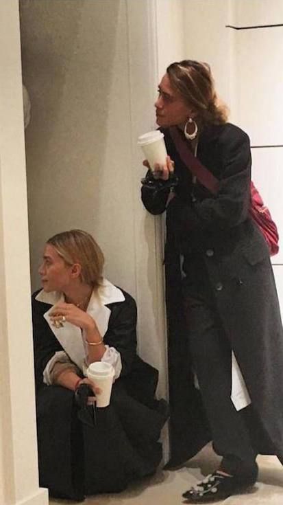 two women standing next to each other in front of a wall and one holding a coffee cup