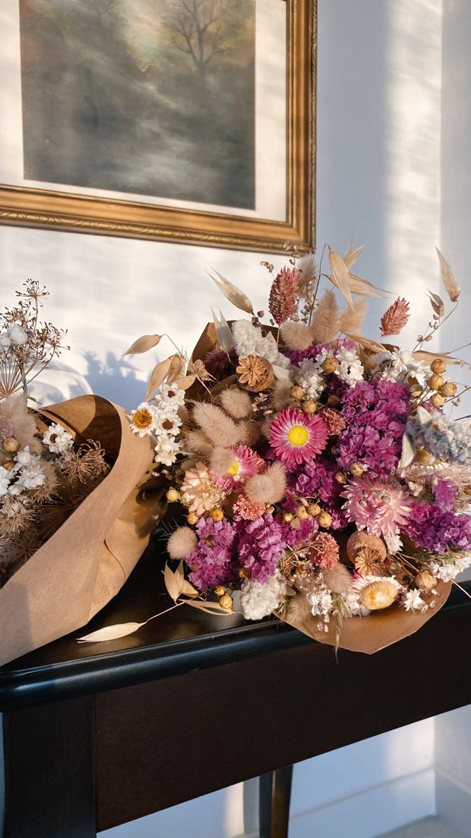 a bouquet of flowers sitting on top of a wooden table next to a framed painting