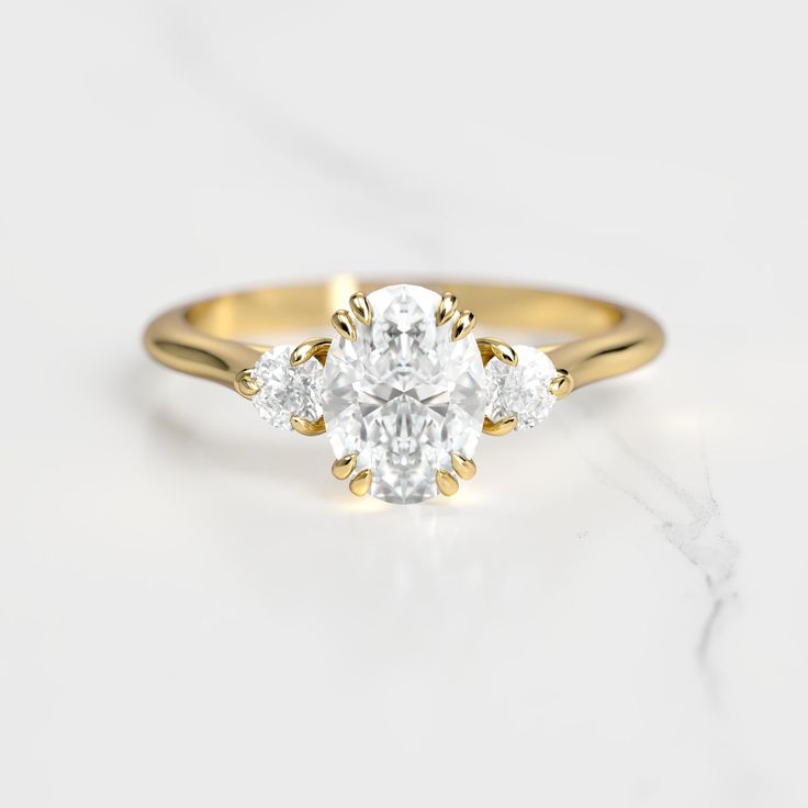 a three stone diamond ring on a marble surface with the center setting in yellow gold