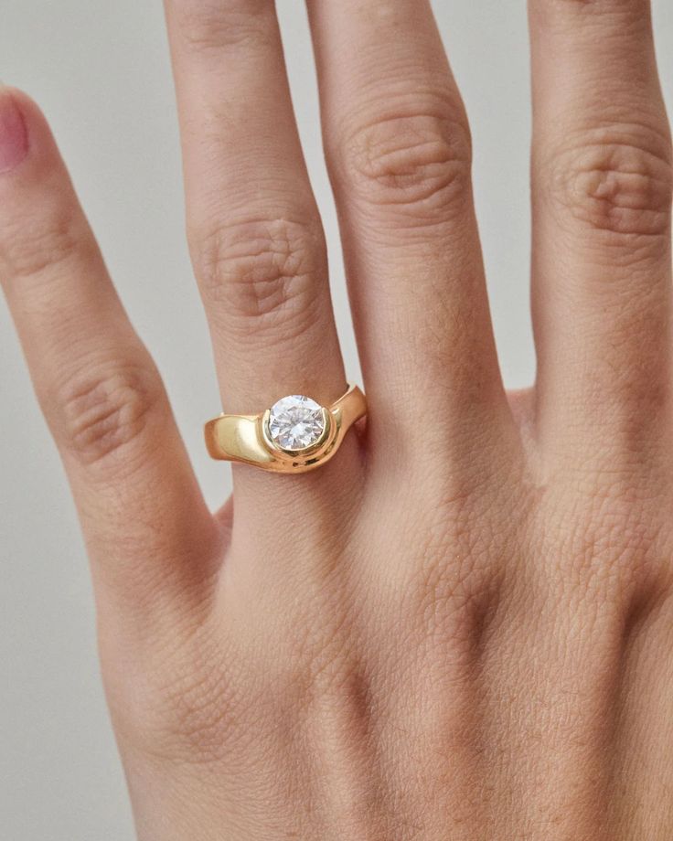 a woman's hand with a gold ring and a white diamond on the middle finger