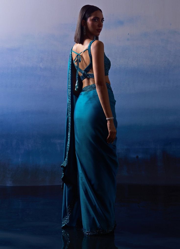 Presenting a stunning Blue Embellished Satin Saree, an epitome of elegance and grace. Crafted from high-quality satin fabric, the blue saree drapes beautifully, enhancing the natural silhouette. The saree is adorned with intricate embroidered tonal sequins, crystals and bugle beads along the borders, adding a touch of sophistication and charm. Paired with a matching, intricately designed modern cut blouse, this ensemble ensures a cohesive and captivating look. Perfect for Sangeet or Wedding Reception or Cocktail, this saree promises to make you the center of attention with its timeless allure. Composition : Saree and Blouse - Satin Care: Dry Clean Only and Vacuum Storage This product can be customized for sleeves, length and colour Delivery : 6-8 weeks as the product is hand crafted. Check