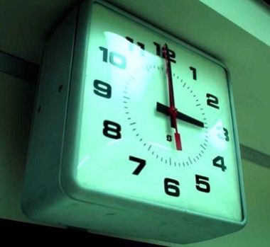 an illuminated clock hanging from the side of a building with red hands and numbers on it