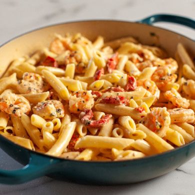 a blue pot filled with pasta and sauce on top of a counter next to a wooden spoon