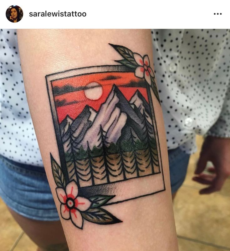 a tattoo with mountains and flowers on the arm