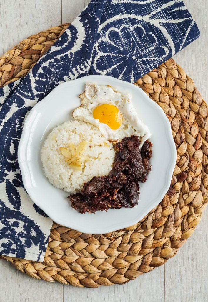 a plate with rice, meat and an egg on it next to a blue napkin