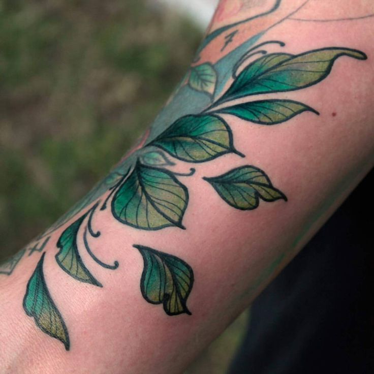 a man's arm with green leaves on it and the word tattoo written in black ink