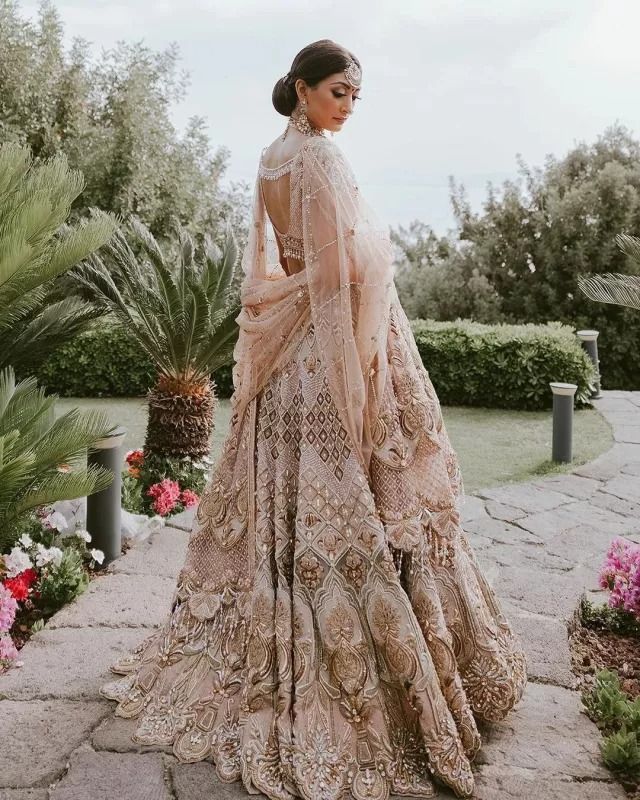 a woman standing in front of some flowers wearing a dress with an intricate pattern on it