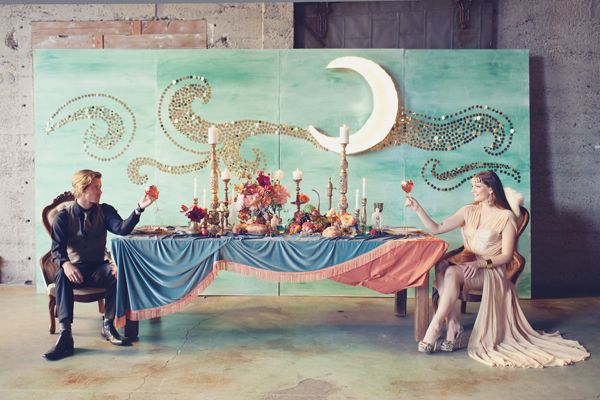 a man and woman sitting at a table in front of a wall with an art work on it