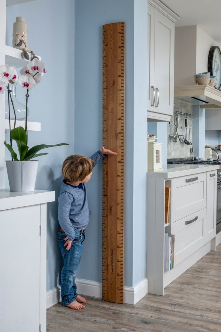 a little boy standing next to a tall wooden ruler in a blue and white kitchen