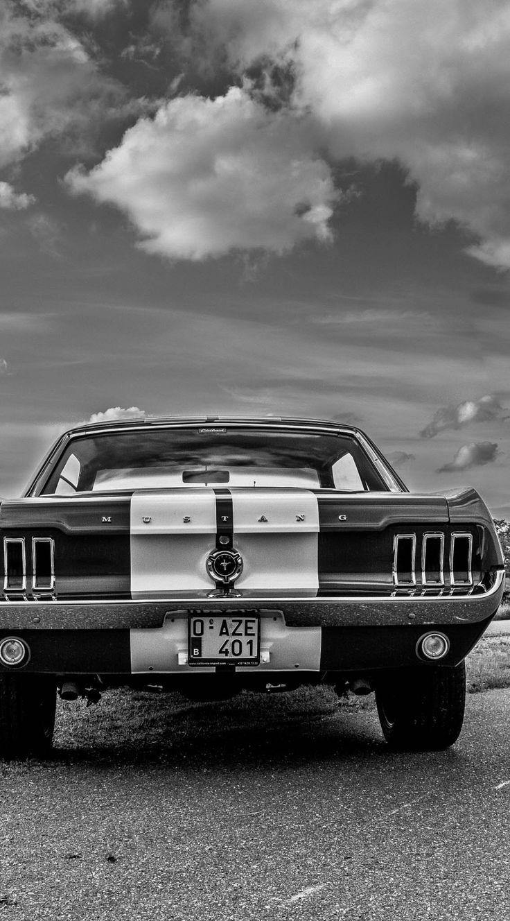 a black and white photo of a car parked on the side of the road with clouds in the background