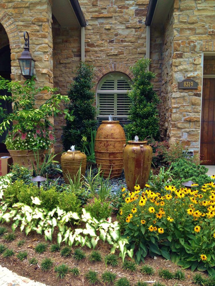 a garden with yellow flowers and large vases in front of a brick building on a sunny day