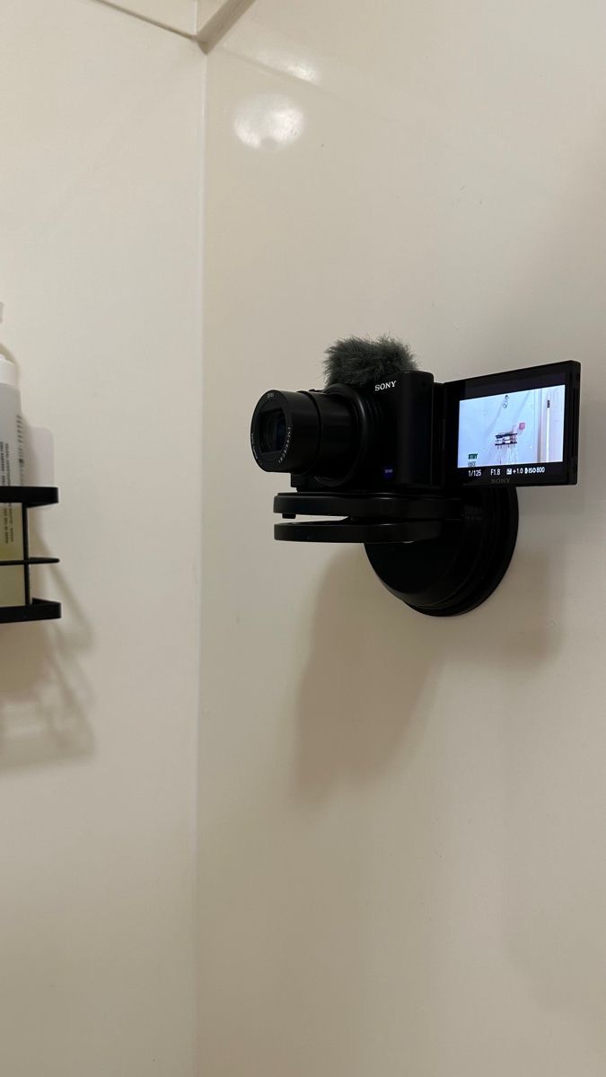 a camera mounted to the side of a white wall next to a black shelf with bottles on it