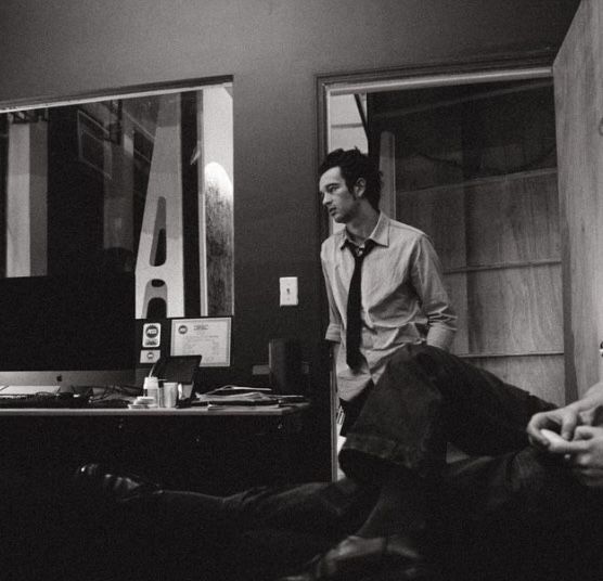 black and white photograph of two men sitting in front of a computer monitor, one with his foot on the desk