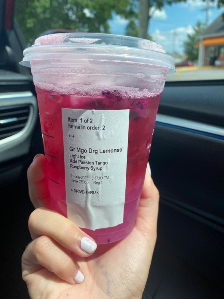 a person holding up a drink in their hand while sitting in the backseat of a car