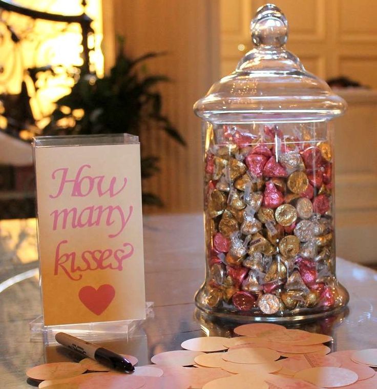 a glass jar filled with lots of candies on top of a table next to a sign that says how many kisses?